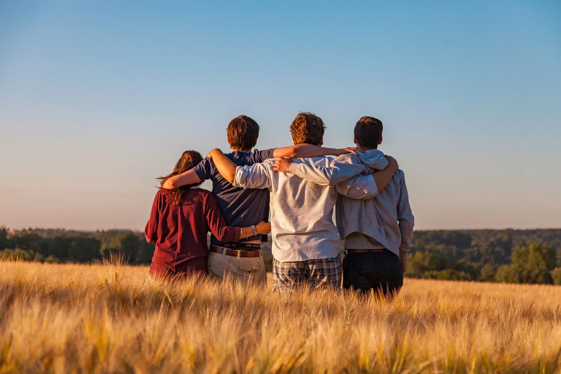 vier junge Menschen von hinten, halten sich an den Schultern