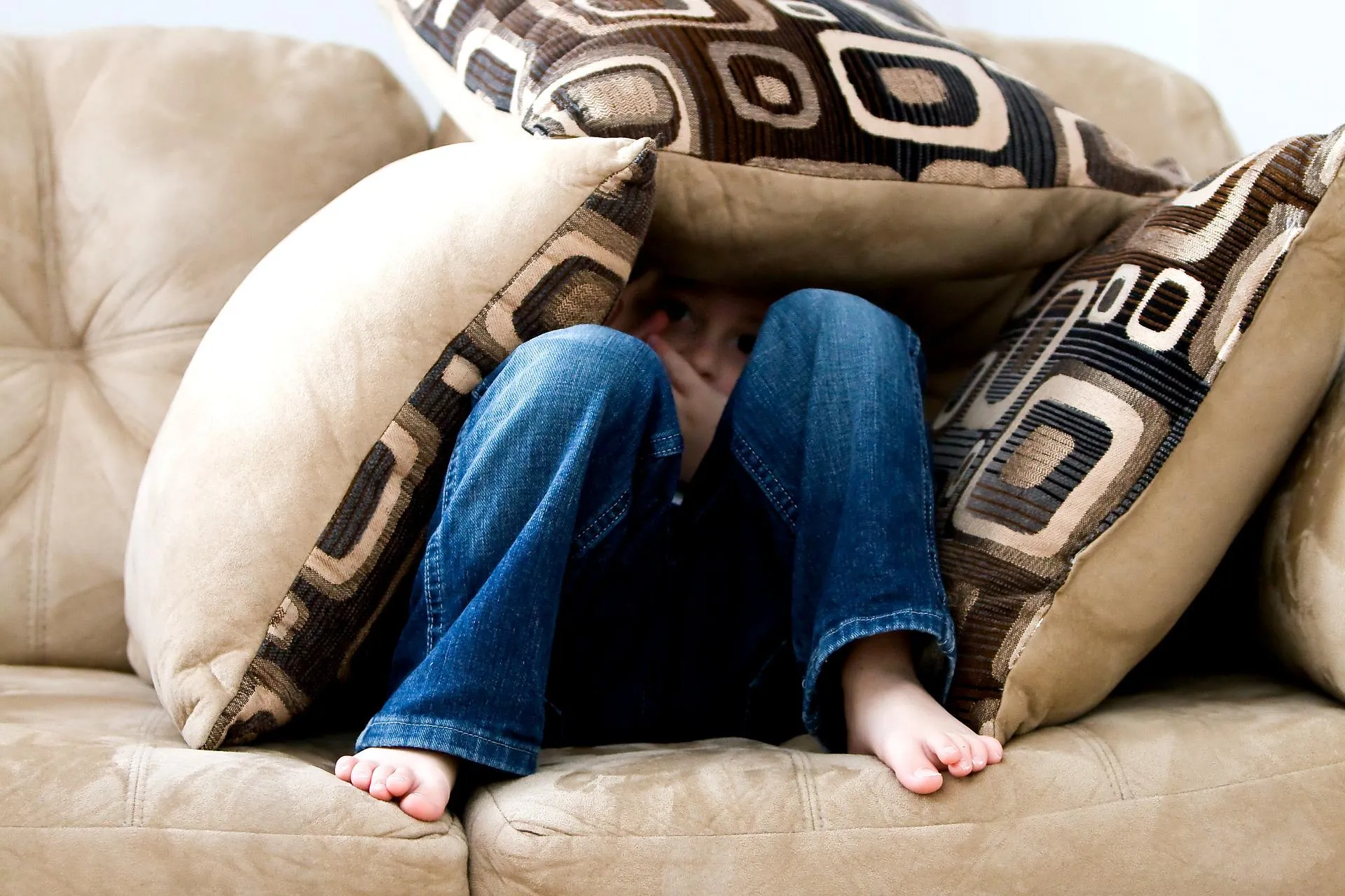 Kind auf Sofa unter Kissen versteckt