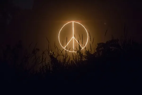 Quelle: unsplash / candice-seplow leuchtendes friedenssymbol auf dunklem Hintergrund