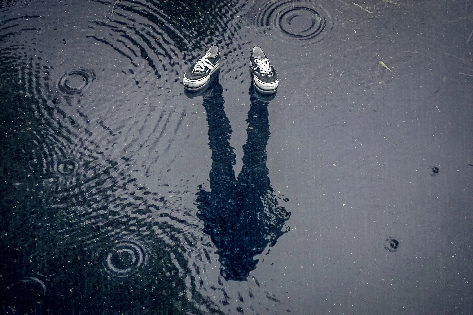 Quelle: pixabay.com / janrye Ein Paar Schuhe stehen in einer Pfütze, in der sich eine Person spiegelt.