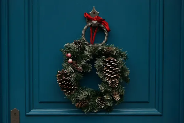 Quelle: Erwan Hesry/Unsplash Winterlicher Kranz aus Tannenzweigen mit Tannenzapfen hängt an blauer Tür