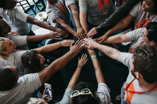 Quelle: Camylla Battani/Unsplash Menschen verschiedener Hautfarbe bilden Kreis, strecken ihre Arme aus, Hände berühren sich