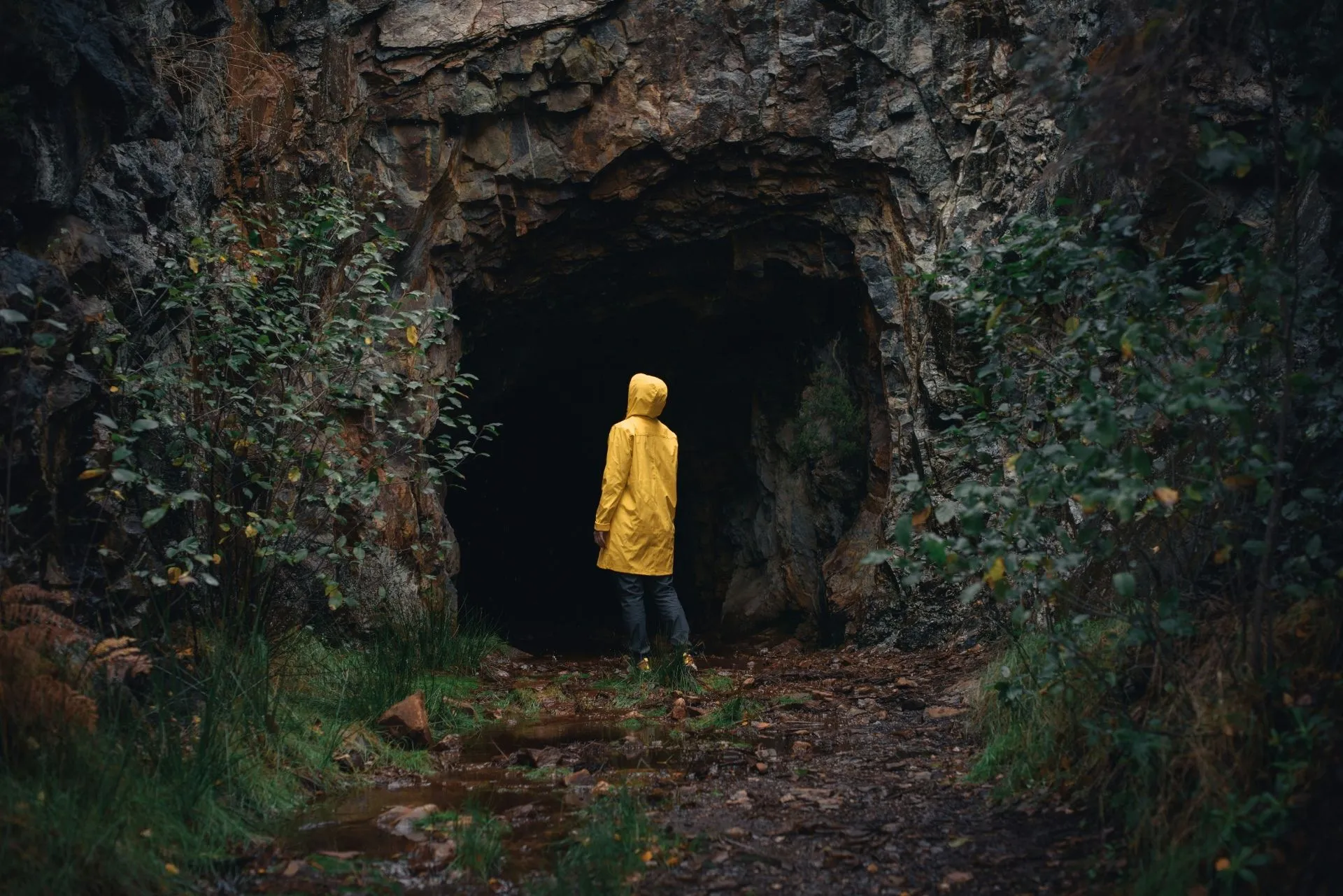 Eine Person in einer gelben Jacke steht vor einer dunklen Höhle