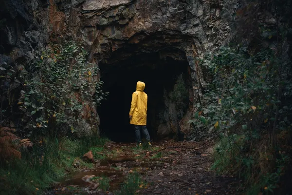 Quelle: Maksym Kaharlytskyi Eine Person in einer gelben Jacke steht vor einer dunklen Höhle