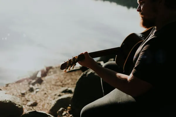 Quelle: Priscilla Du Preez / Unsplash Mann sitzt am Ufer und spielt Gitarre