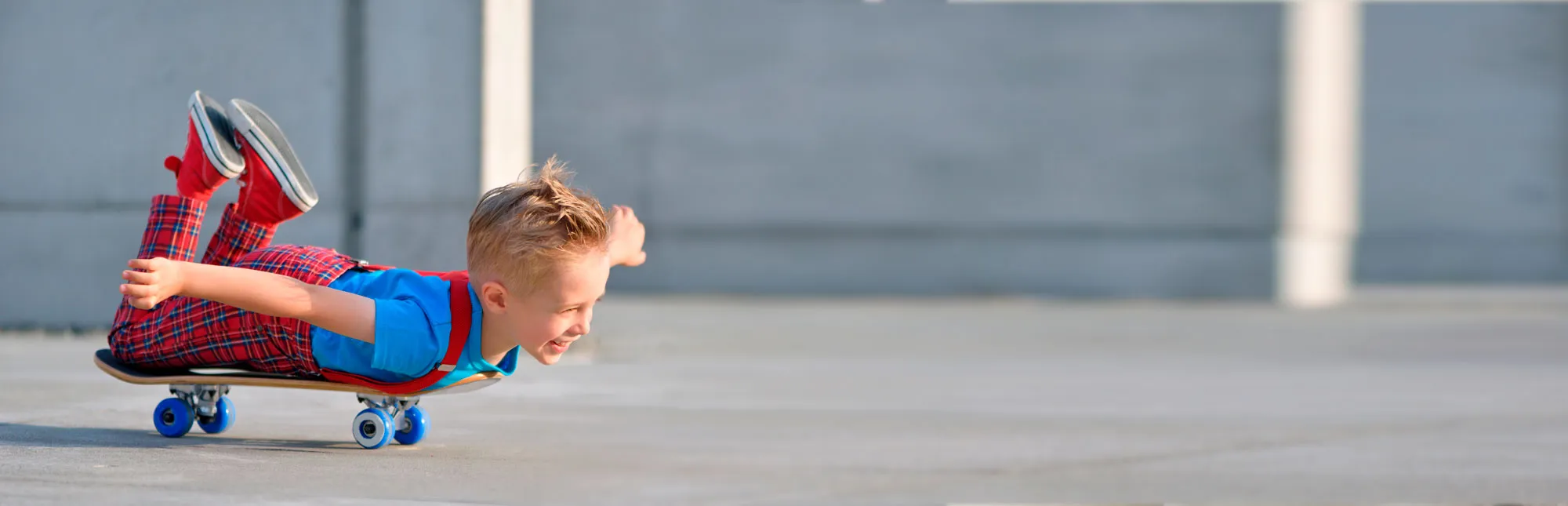Kleiner Junge liegt auf einem Skateboard und fährt damit