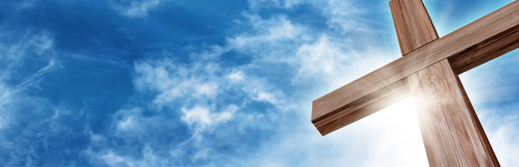 Quelle: Balazs – stock.adobe.com Blick von unten auf ein großes Holzkreuz vor einem leicht bewölkten Himmel