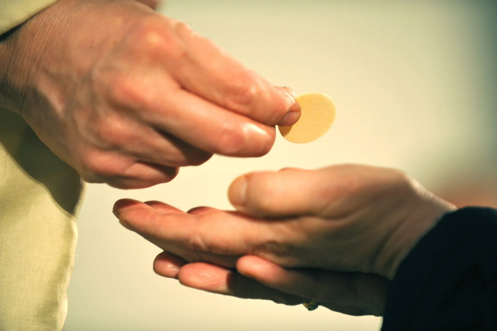 Man sieht, wie ein Pfarrer einem Kirchenbesucher eine Oblate in die Hand legt