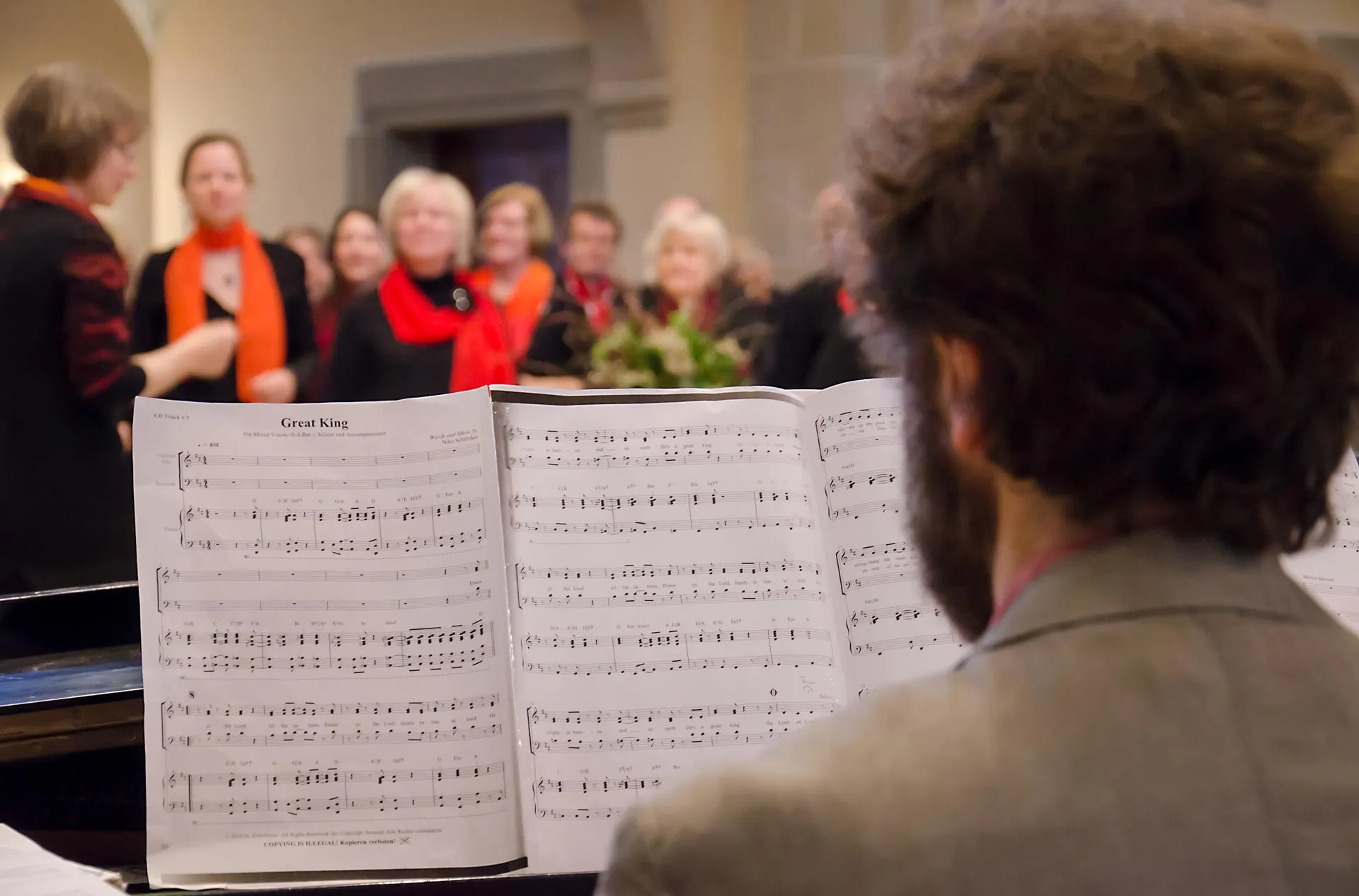 Blick über die Schulter eines Pianisten, im Hintergrund unscharf ein Chor