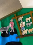 Godly Play Material zum Gleichnis vom guten Hirten: grüne Filzunterlage, Filzstreifen als Gatter, blaues Filzstück als Wasser, 3 schwarze Filzstücke als Symbol für gefährliche Orte, 2 Hirtenfiguren aus Holz, 5 Holzschafe, 1 Wolf aus Holz