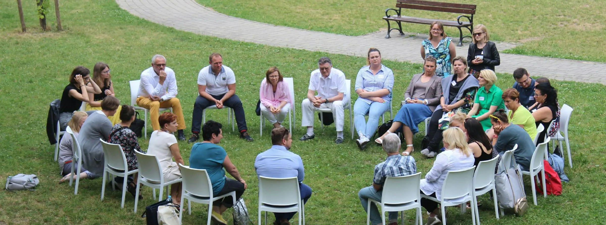 Quelle: dorota-trzaska-1tAtO-9HYNM-unsplash Gruppenbild Worksop aller Teilnehmenr sitzen in einem Stuhlkreis auf einer Wiese