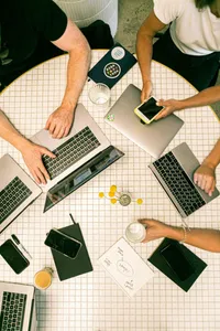 Ausschnittsbild: Blick von oben auf einen runden Tisch mit Laptops und Menschen, die darum sitzen
