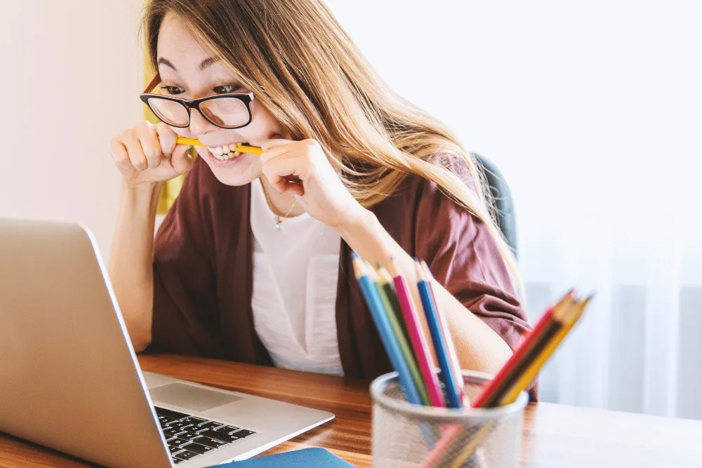 Frau vor einem Laptop, die auf einem Bleistift kaut