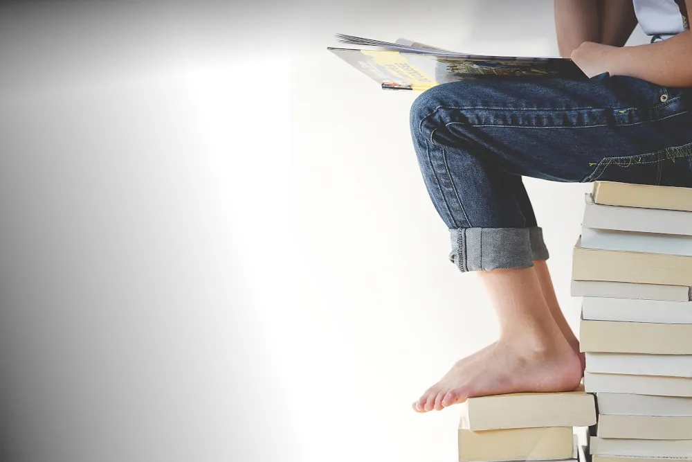 Quelle: Pexels/Pixabay Person sitzt auf Bücherstapel und liest