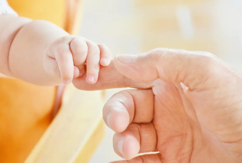 Baby hält sich am Finger eines Erwachsenen fest.